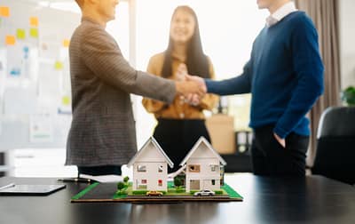 Property management agreement — landlords and agents shaking hands with model houses in foreground, representing Brighton & Hove lettings